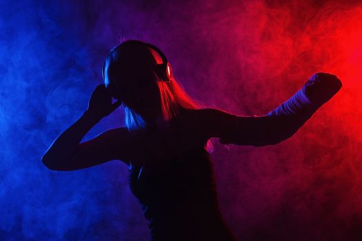 sexy girl with broken arm listening music on headphones and dancing, disco smoke in the background