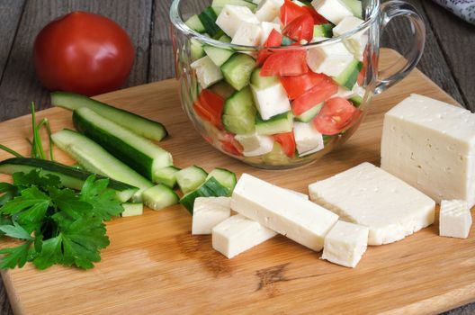 Salad with vegetables and cheese, and ingredients on the cutting Board. Grey wooden background.