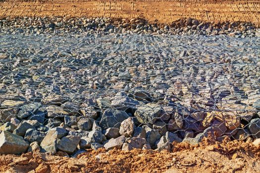 Preparation of the river bank near village for protection against a flood.Construction of the dam - granite boulders piled in metall grid on the surface of the dam.