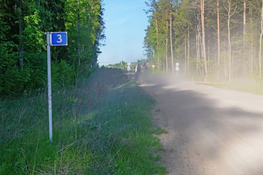 Left photo road sign - 3 kilometers. Over the road a cloud of dust from the traveling vehicle.