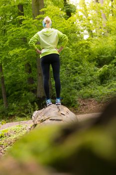 Active sporty woman standing on tree trunk while workout in nature. Wellness and healthy lifestyle concept.