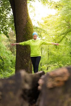 Active sporty woman holding balance on tree trunk while workout in nature. Wellness and healthy lifestyle concept.