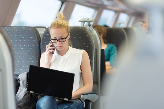 Businesswoman talking on cellphone and working on laptop while traveling by train. Business travel concept.