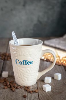 Mug of coffee on the old Board, spilled coffee beans and sugar cubes. Morning light