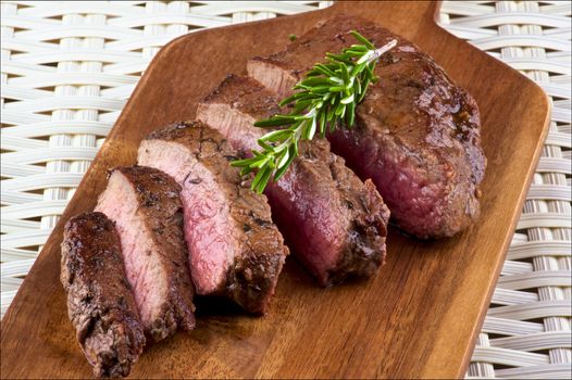 Slices of Delicious Roast Beef Medium Rare with Rosemary on Wooden Cutting Board closeup on Wicker background