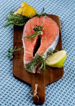 Perfect Raw Salmon Steak with Lemon, Rosemary and Thyme on Wooden Cutting Board closeup on Blue Napkin background