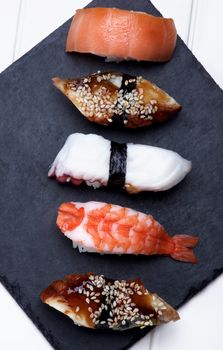 Various Sashimi Sushi with Shrimp, Octopus, Smoked Eel and Salmon In a Row on Stone Plate closeup on White Plank background