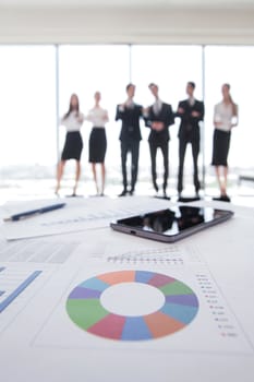 Close-up of financial reports and tablet, business people team standing in the background