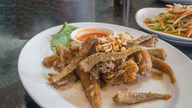 Fried fish topped with garlic served on dish with chili sauce