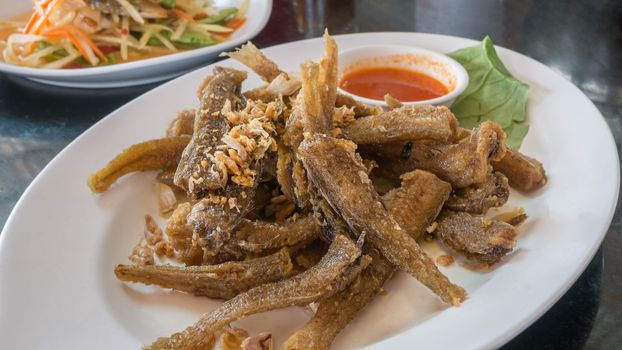 Fried fish topped with garlic served on dish with chili sauce