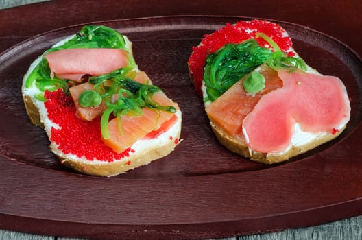 Two colourful sandwiches with seafood lay on a wooden tray