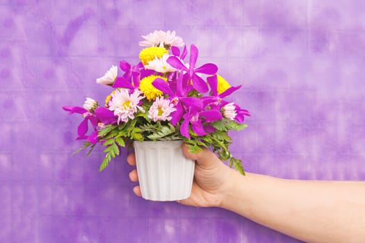 Hand holding bouquet of chrysanthemum and orchid flowers isolated on violet background.