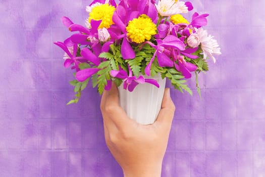 Hand holding bouquet of chrysanthemum and orchid flowers isolated on violet background.