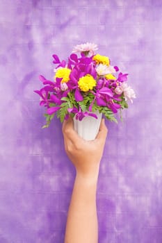 Hand holding bouquet of chrysanthemum and orchid flowers isolated on violet background.