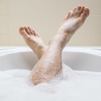 Men's feet in a bright white bathtub, selective focus on toes