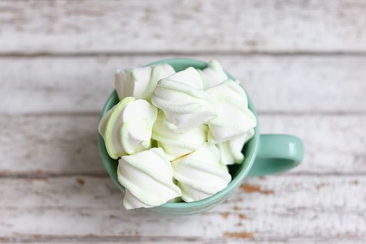 Peppermint large marshmallows in a large green cup on white wooden background