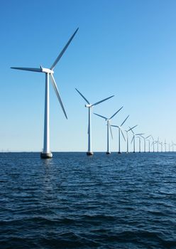Vertical perspective line of ocean windmills with dark water and sky