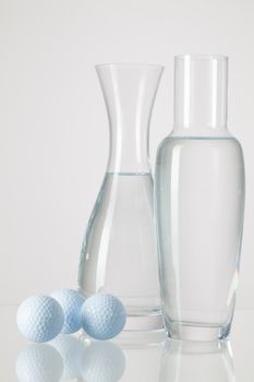 Two vases with clean water and golf balls on a glass table