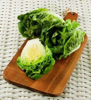 Fresh Crunchy Romaine Lettuce Two Full Heads and Half on Wooden Cutting Board closeup on Wicker background