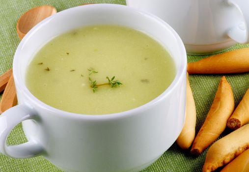 Delicious Asparagus Cream Soup in White Soup Cups with Bread Sticks and Wooden Spoons Cross Section on Green Napkin