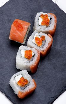 Gourmet Sushi with Smoked Sliced Salmon and Gourmet Red Caviar on Stone Plate closeup on White Plank background. Top View