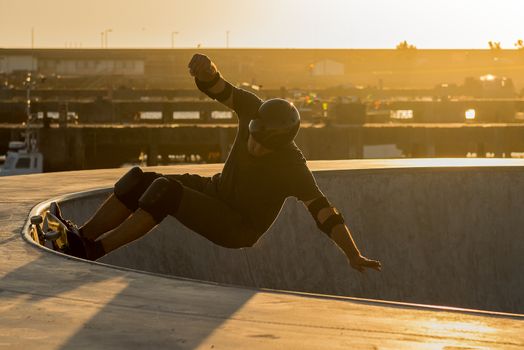 Skateboarder in a concrete pool at skatepark on a beatiful sunset.