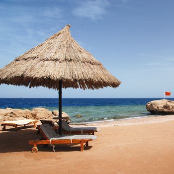 Photo of beautiful clear turquoise sea ocean water surface with ripples low waves on seascape background and sunbed under parasol on the sand beach.