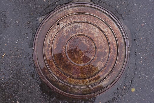 Closeup photo of Old Sewer rust manhole cover on the urban asphalt road. Rain scene