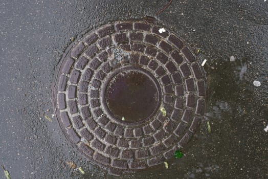 Closeup photo of Old Sewer rust manhole cover on the urban asphalt road. Rain scene