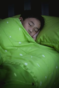 Healthy child. Little asian boy sleeping peacefully on bed in dark bedroom. Vignette picture style.