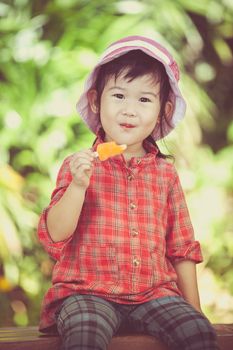 Little asian girl wearing pink hat and eating ice cream in the summer on blurred nature background. Pretty child in nature. Outdoors. Cross process.