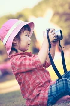 Cute little asian girl taking photos using vintage film camera in the park on blurred background, summer in the day time. Adorable child in nature, outdoors. Vintage style.