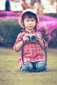 Cute little asian girl holding vintage film camera in the park on blurred background, summer in the day time. Adorable child in nature, outdoors. Vintage style.