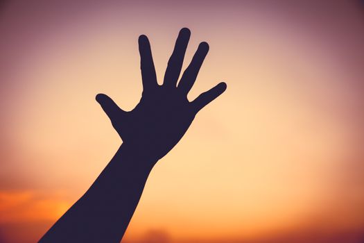 Silhouette of a hand on colorful sunset sky background. Symbol is mean to say hi , five , hand up, stop. Outdoors.