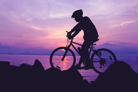 Silhouette of bicyclist riding the bike on a rocky trail at seaside, on colorful sunset sky background. Active outdoors lifestyle for healthy concept. Vintage style.