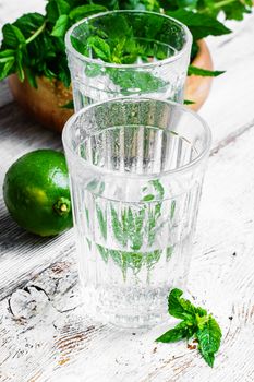 Drinking water in glass and lime and mint on light background