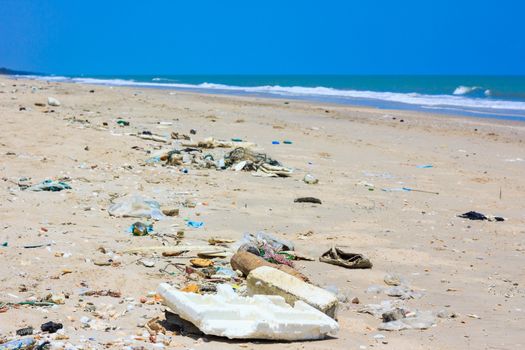 Pollution on the beach of tropical sea. Plastic garbage, foam, rubbish and dirty waste on beach in summer day. The sky above is a perfect blue color. Outdoors