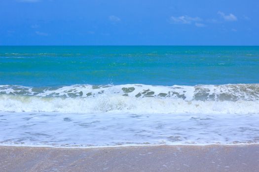 A tranquil sea scene. The waves crashing roll in and out are foamy. Beautiful seashells on beach, the water is a crystal-blue color. The sky above is a perfect blue color.