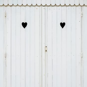 Detail of white wooden beach hut with two carved hearts in the doors.