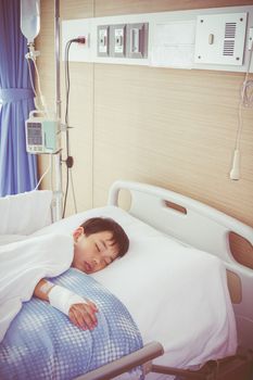 Illness asian boy sleeping on sickbed in hospital with infusion pump intravenous IV drip. Health care and people concept. Vintage style.