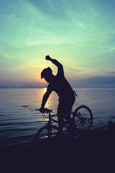Silhouette of bicyclist riding the bike on rocky trail at seaside, on colorful sunset sky background. Active outdoors lifestyle for healthy concept. Action of winner or successful people.