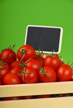Fresh red ripe cherry tomatoes in small wooden box with black chalkboard price sign tag over green background
