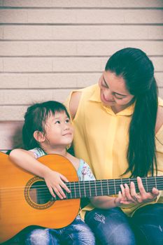 Happy family spending time together at home. Asian mother with daughter playing classic guitar. Positive human emotion. Vignette and vintage style.