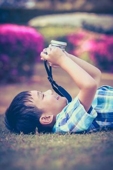 Handsome asian boy taking photo by vintage film camera, exploring nature at park, on summer in the day time. Child in nature, outdoors. Active lifestyle, curiosity, pursuing a hobby concept. Vintage.