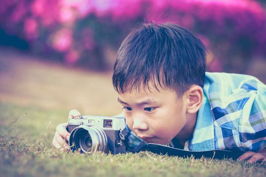 Asian boy taking photo by vintage film camera on blurred nature background at the day time. Adorable child enjoying at park. Outdoors. Vintage picture style.