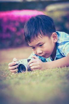 Asian boy taking photo by vintage film camera on blurred nature background at the day time. Adorable child enjoying at park. Outdoors. Vignette and vintage picture style.