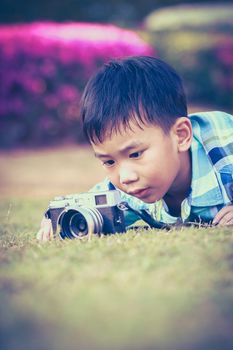 Asian boy taking photo by vintage film camera on blurred nature background at the day time. Adorable child enjoying at park. Outdoors. Vignette and vintage picture style.