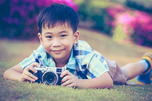Handsome asian boy taking photo by vintage film camera, exploring nature at park, on summer in the day time. Child in nature, outdoors. Active lifestyle, curiosity, pursuing a hobby concept. Vintage.