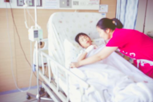Blurred background of illness asian child admitted at modern and comfortable equipped hospital room. Mother take care her son. Health care and people concept. Vintage style.