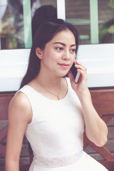 Asian young woman talking on mobile phone outside on home summer. Active lifestyle happy young adult on relaxing day at home. Vintage tone.
